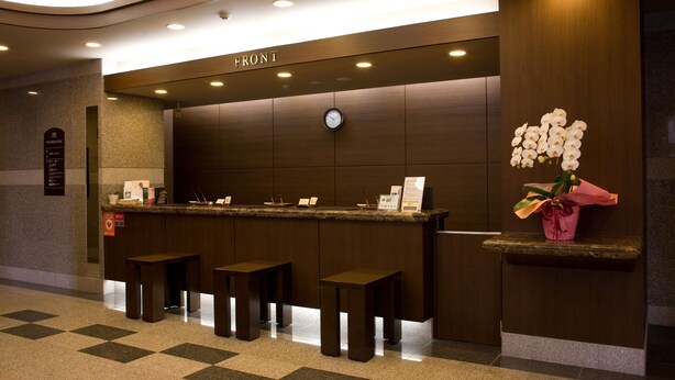 A reception desk with a clock, a sign reading "FRONT", and a vase of white orchids. There are three wooden stools in front of the desk.