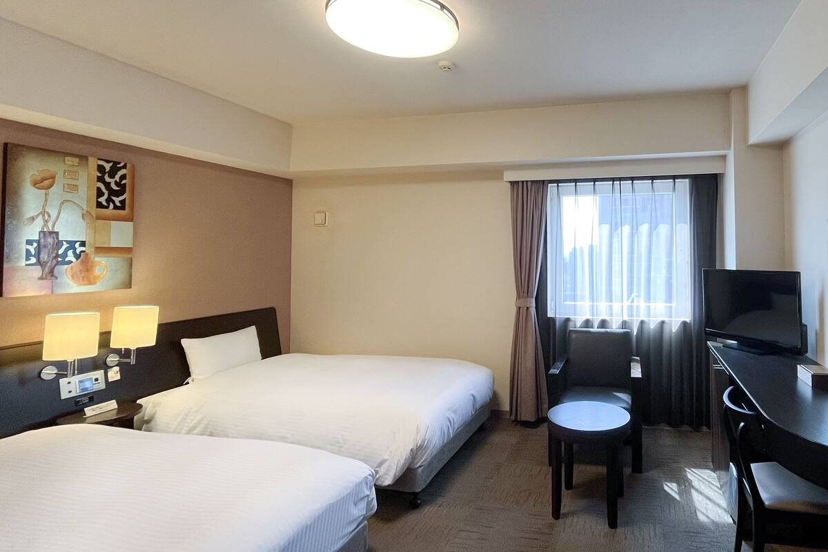 A hotel room with two beds, a desk with a chair, a television, and a painting on the wall.