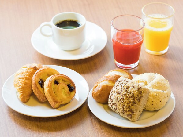 A breakfast setting with croissants, a cup of coffee, and glasses of juice on a wooden table.