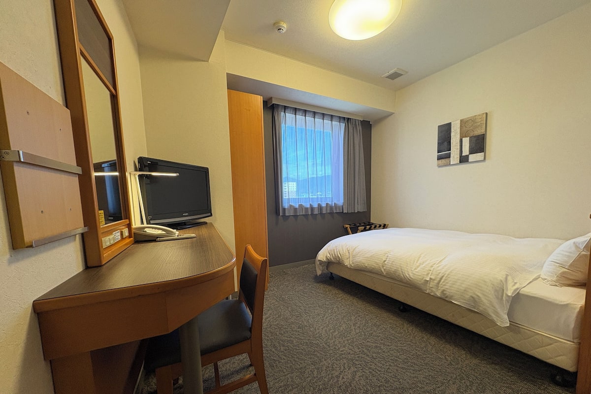 Habitación de hotel con escritorio, silla, cama y ventana con cortinas.