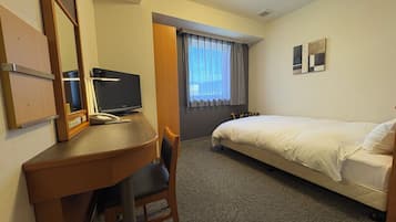 Habitació d'hotel amb escriptori, cadira, llit i finestra amb cortines.