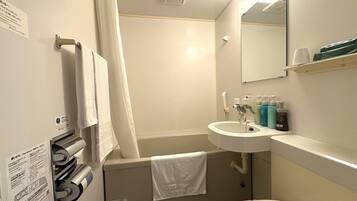 Un baño con lavamanos, espejo y ducha. Hay toallas colgadas en la pared y un estante con artículos de aseo.