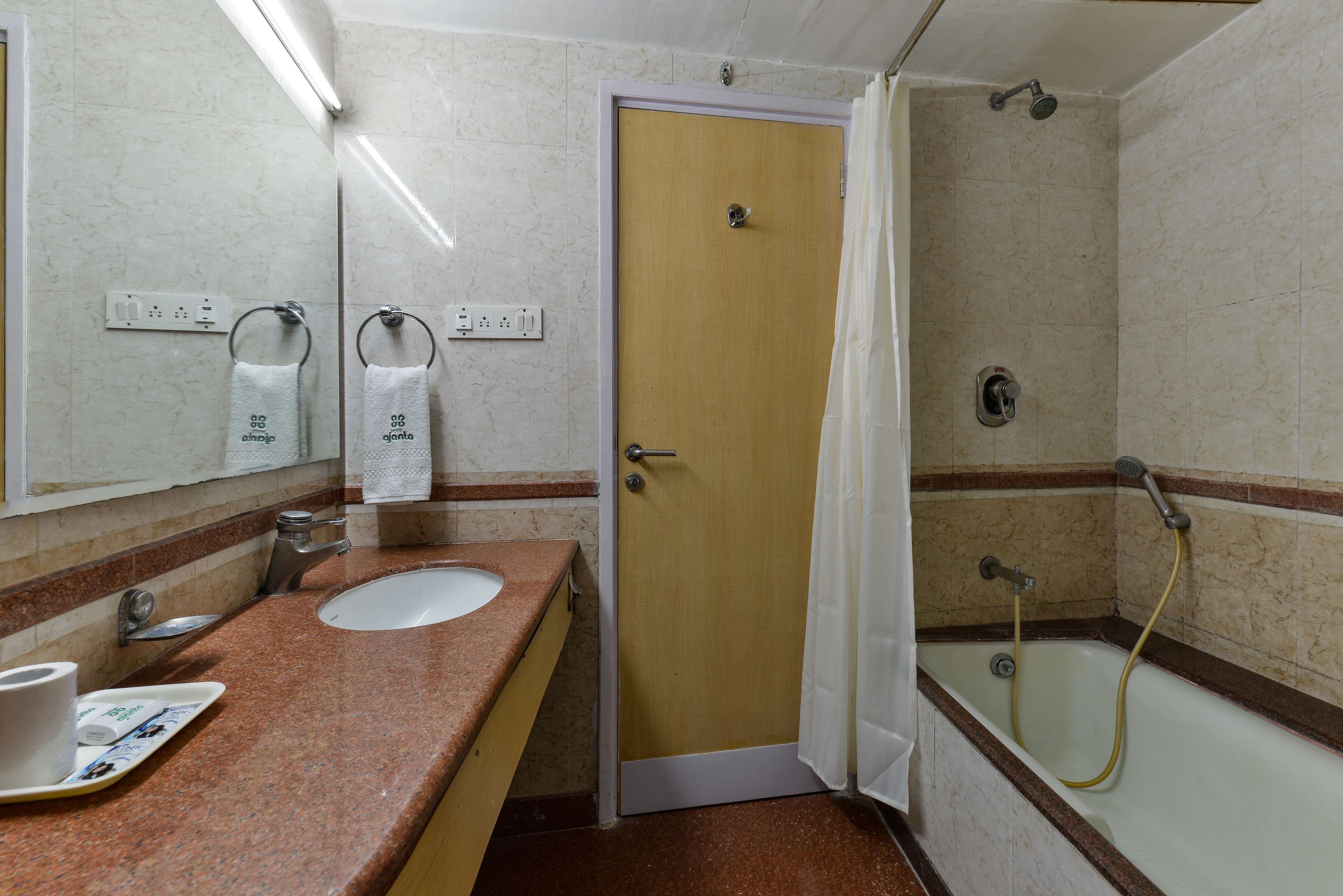 A bathroom with a sink, mirror, towel dispenser, and shower.