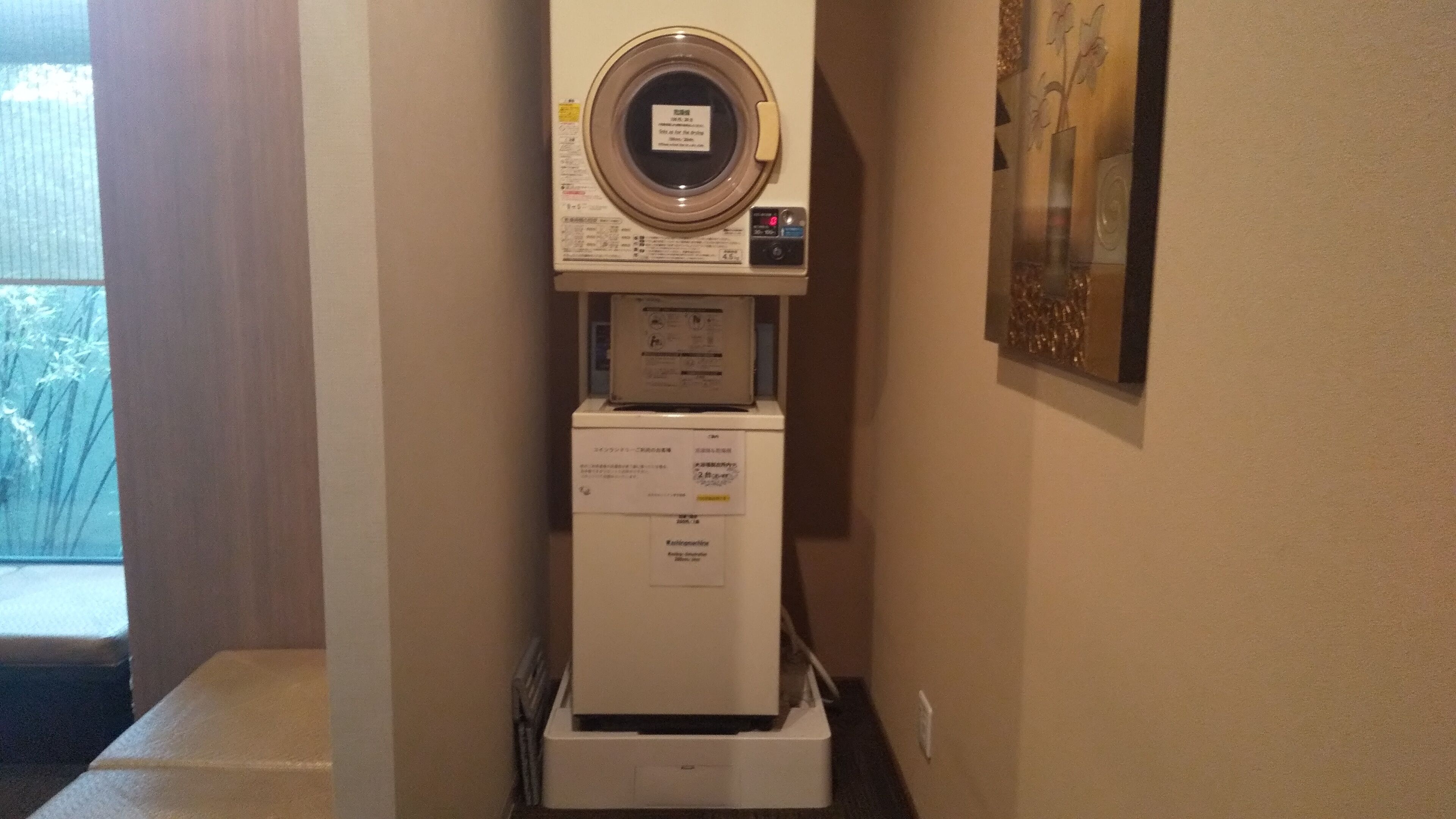 A compact, wall-mounted washing machine with a control panel and a small refrigerator below it.