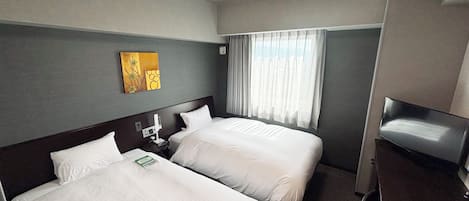 Una habitación de hotel con dos camas, una mesita de noche con teléfono y lámpara, una ventana con cortinas y un cuadro en la pared.