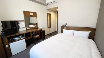 A hotel room with a bed, a desk with a television, a mirror, and a small refrigerator.