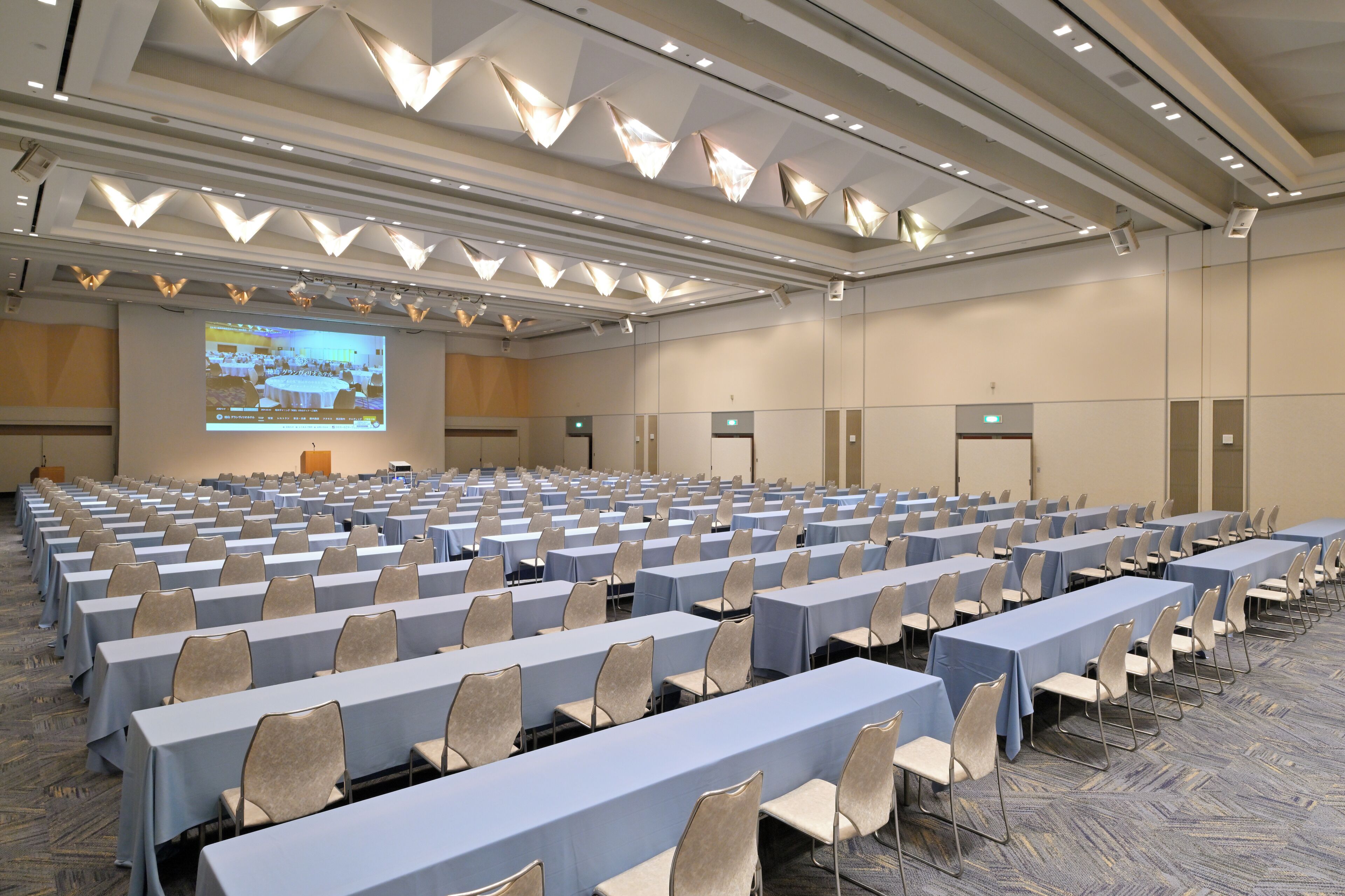 A large conference room with rows of tables and chairs, a projection screen, and a podium.