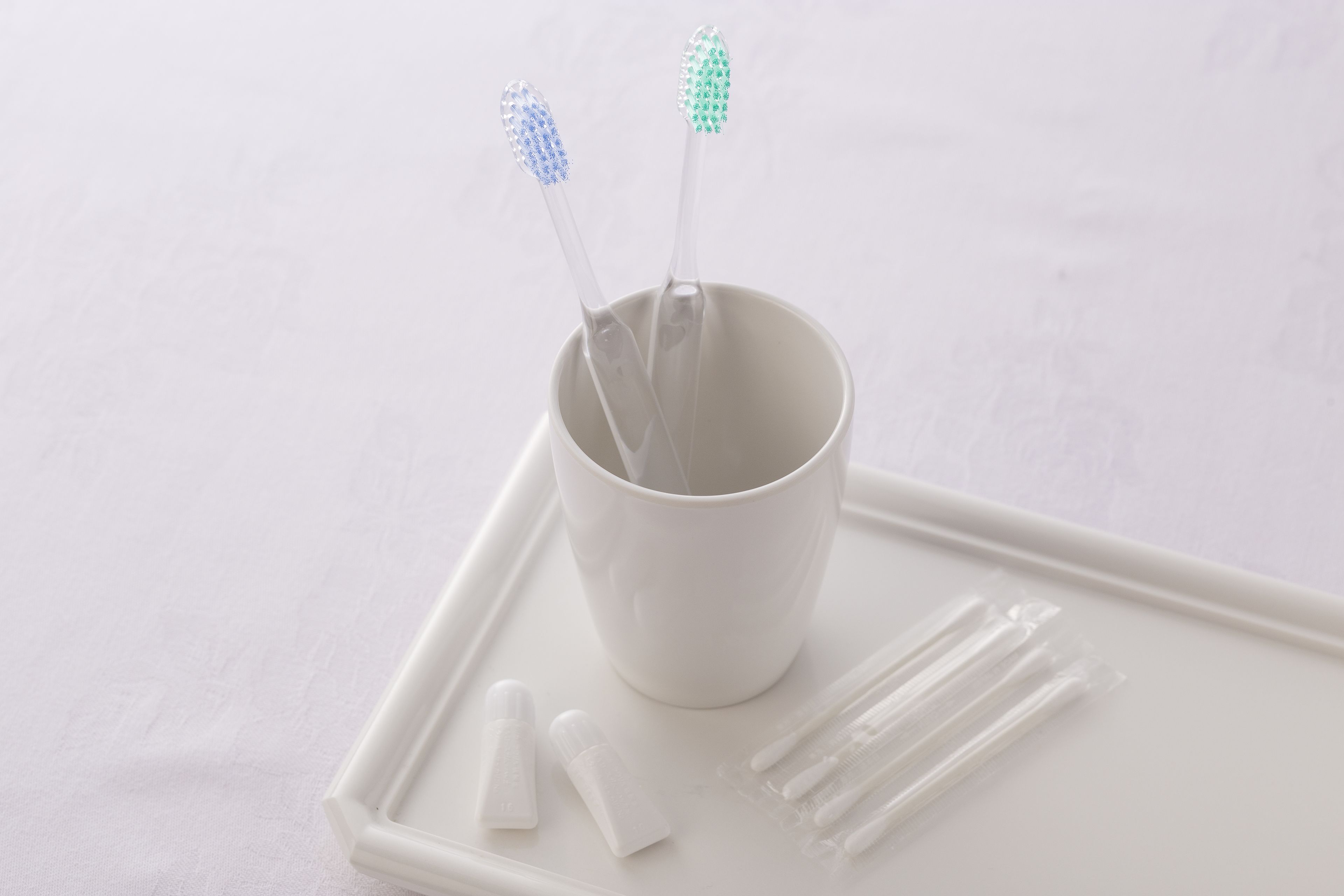 A white cup with two toothbrushes and dental floss on a tray.