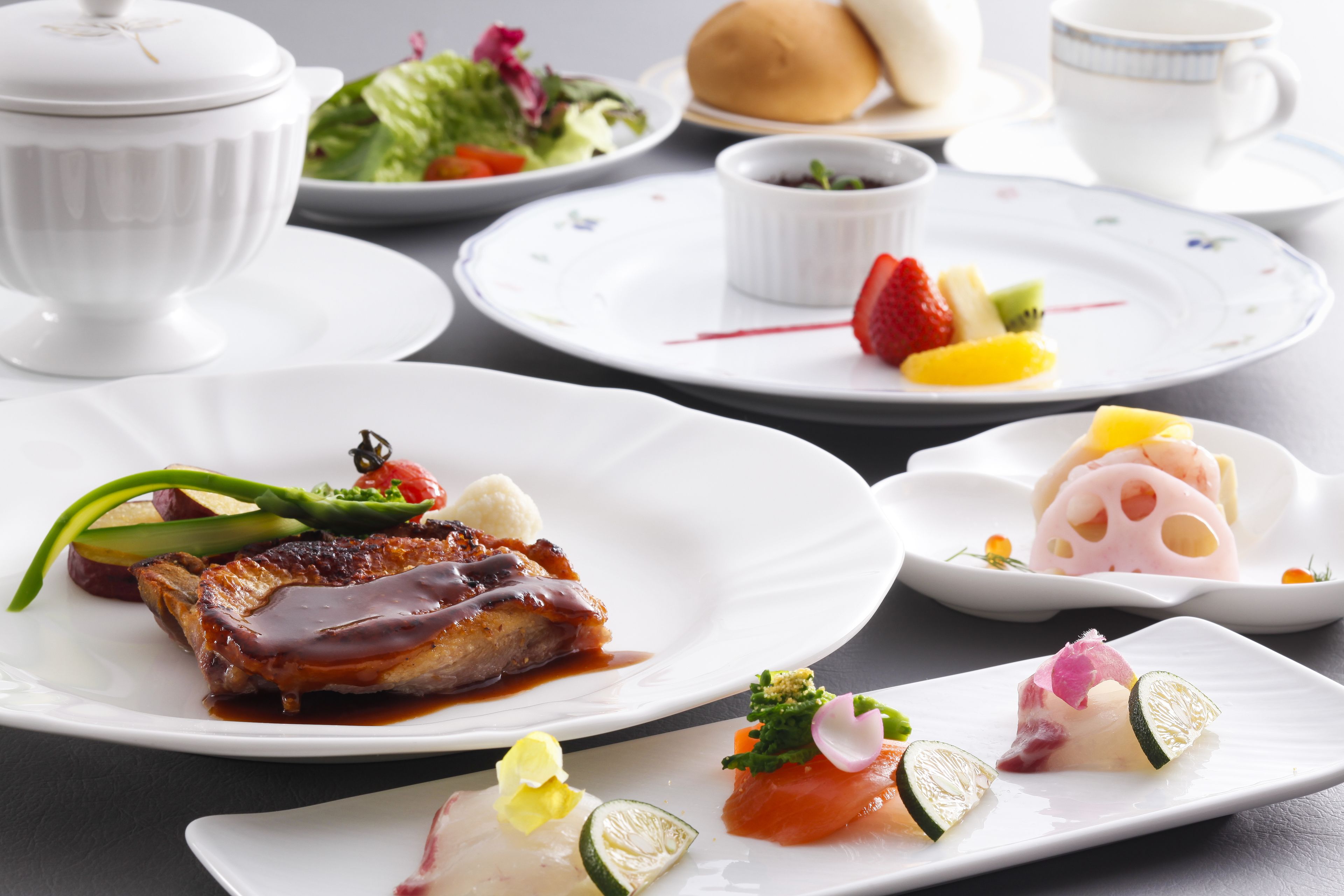 A variety of dishes on white plates, including a steak with sauce, a dessert with fruit, and a dish with salmon and vegetables.