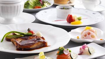 A variety of dishes on white plates, including a steak with sauce, a dessert with fruit, and a dish with salmon and vegetables.