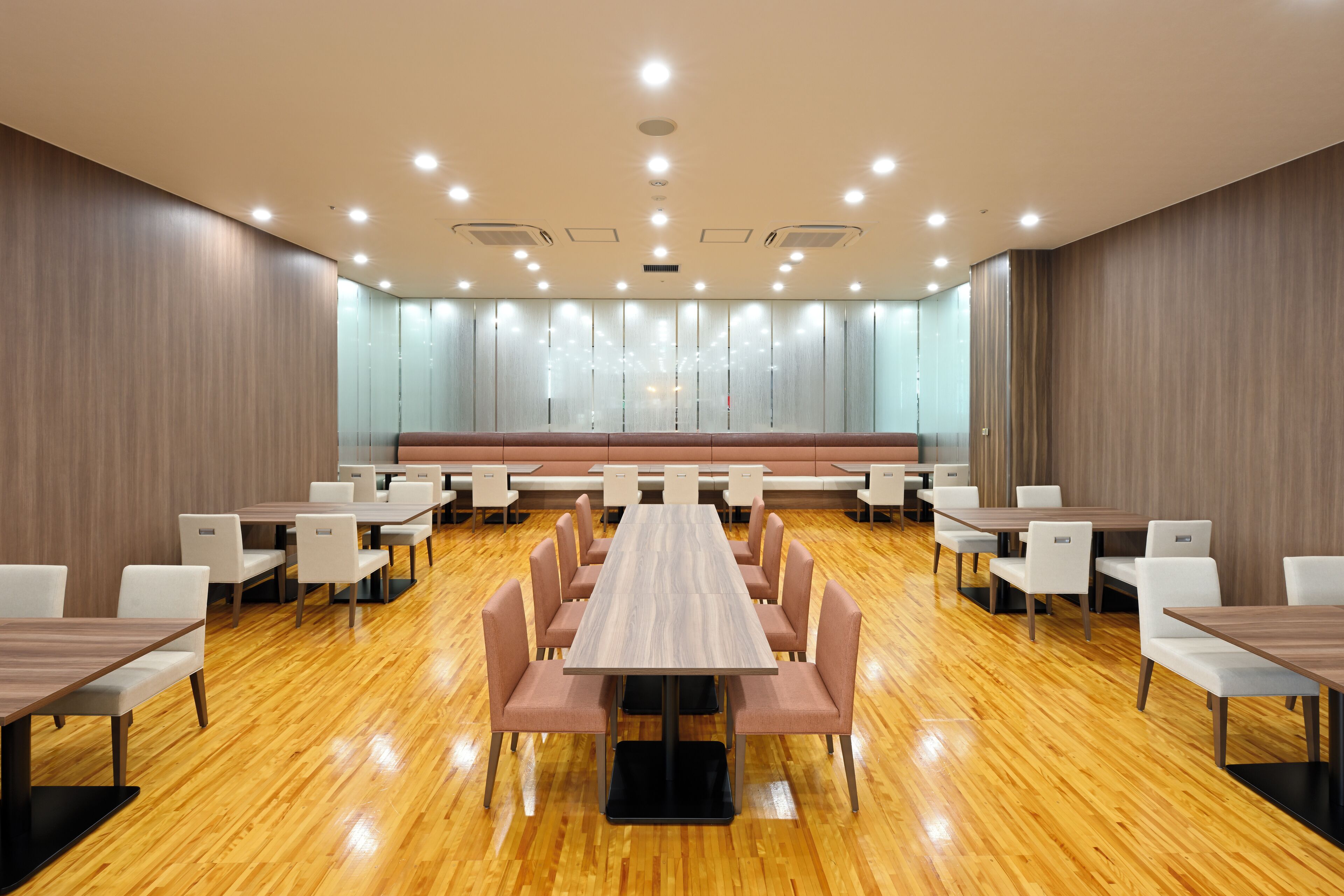 A conference room with a long table surrounded by chairs, wooden floors, and recessed ceiling lights.