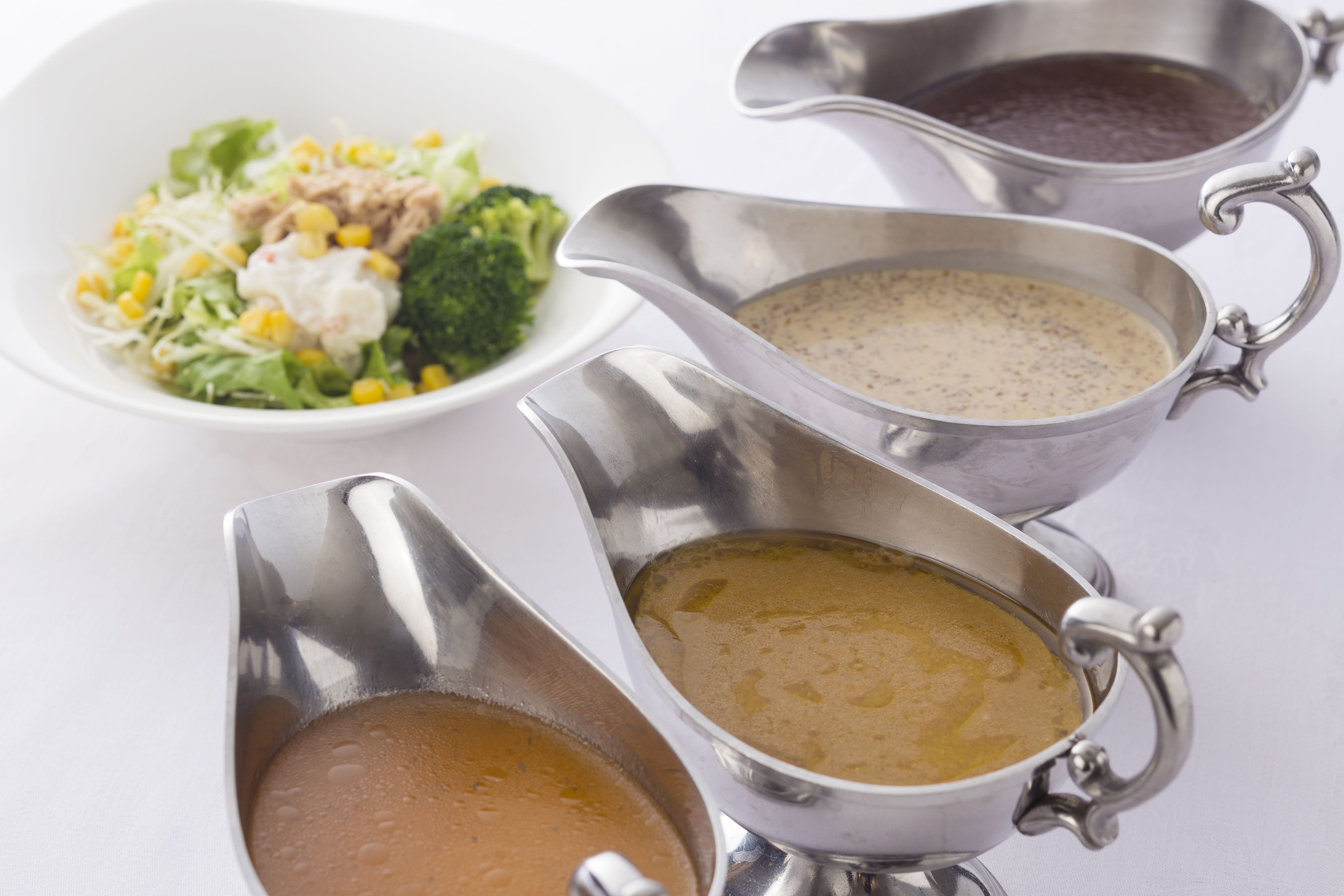 A white table with four metal gravy boats containing different types of gravy.