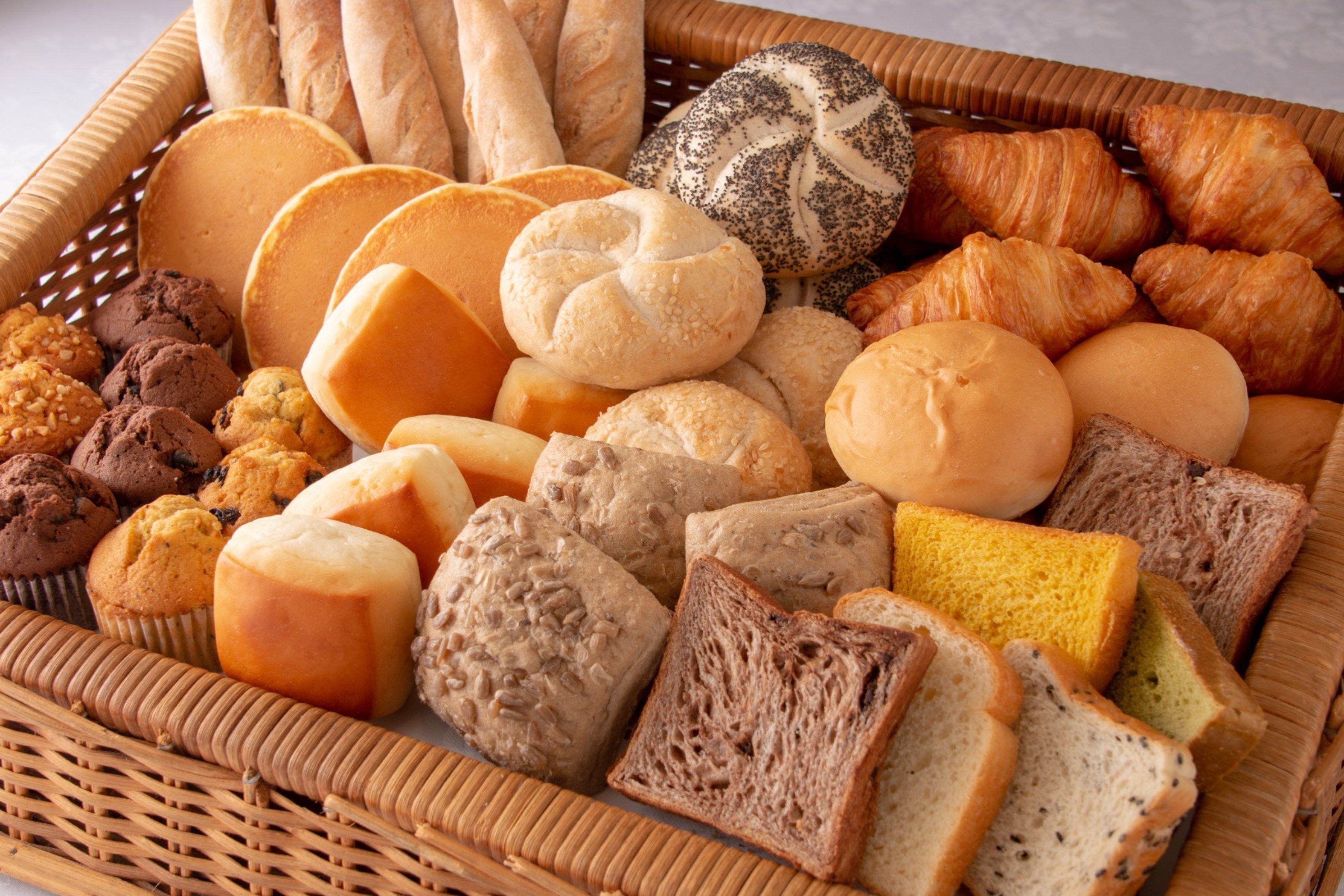 A wicker basket filled with various breads, pastries, and cookies.