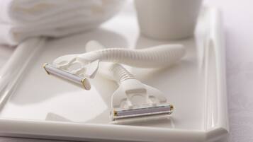A white tray with a razor and a razor case, a folded white towel, and a white cup.