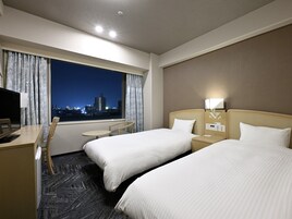 Habitación de hotel con dos camas, un escritorio, una silla, una mesita y una ventana con cortinas.