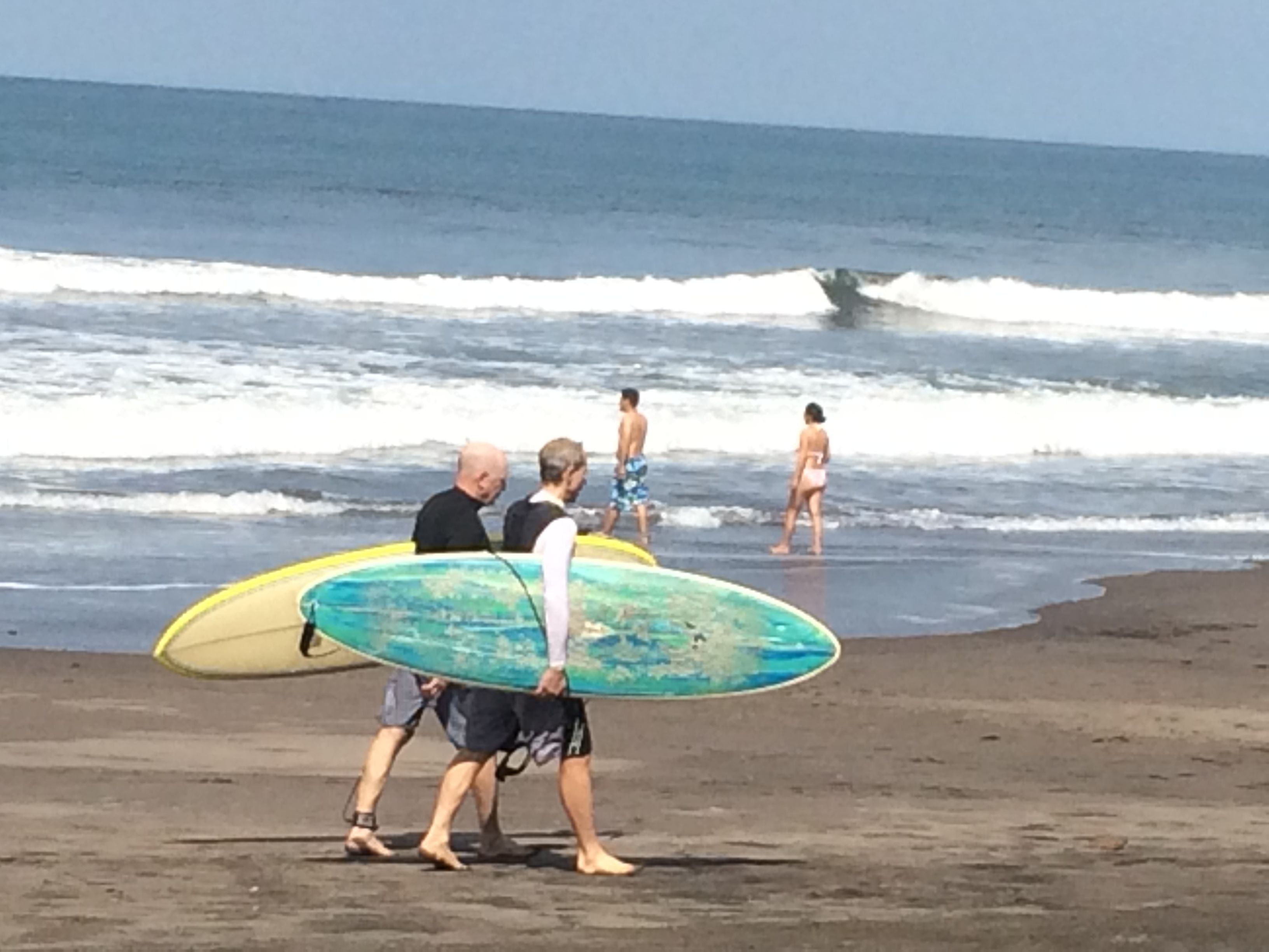 Eine Strandansicht mit Menschen, die entlanggehen und Surfbretter tragen.