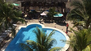 Zona de piscina con una estructura de techo de paja, palmeras y vistas a la playa.
