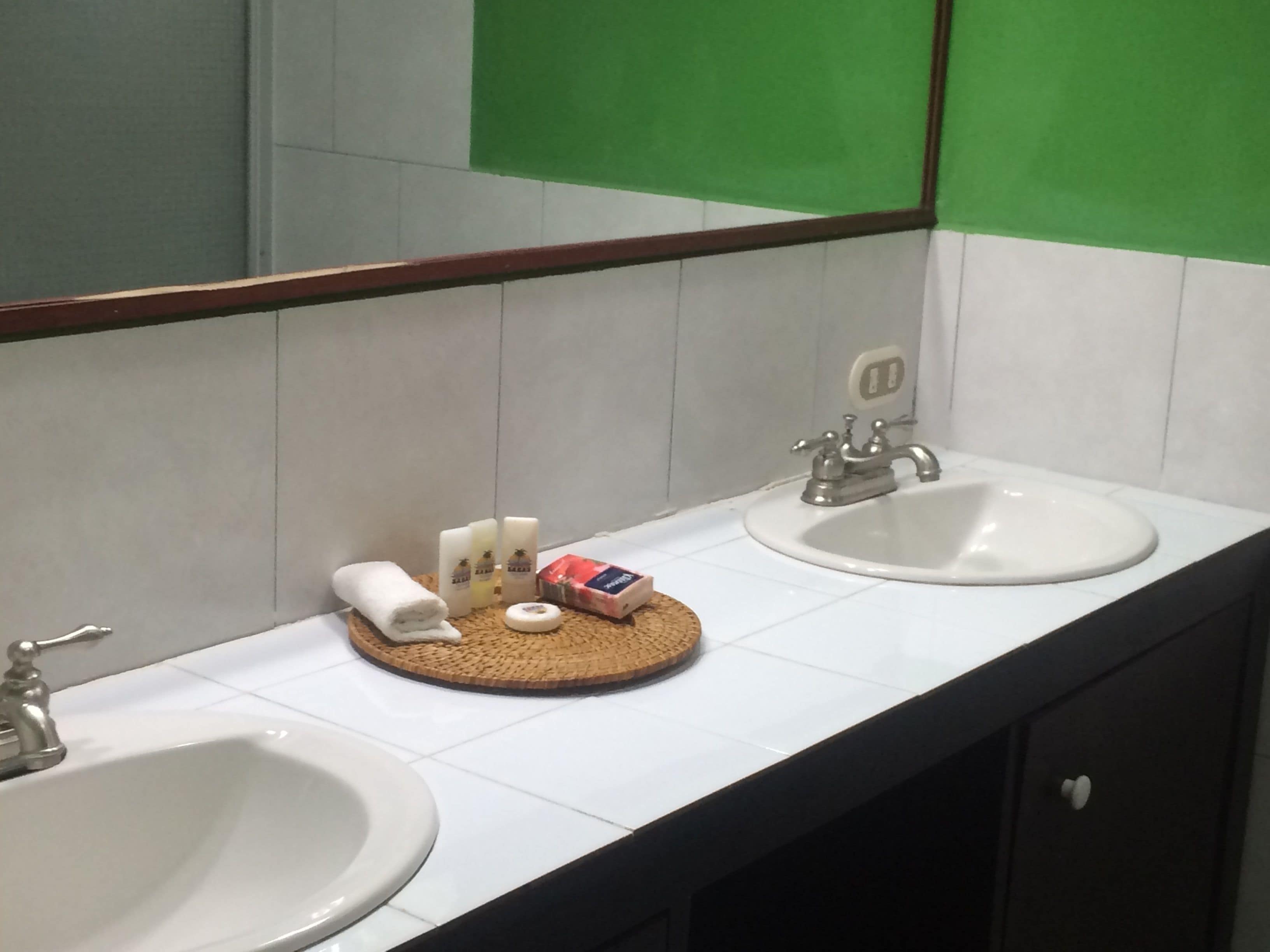 Un baño con dos lavamanos, un espejo y artículos de aseo en una bandeja.