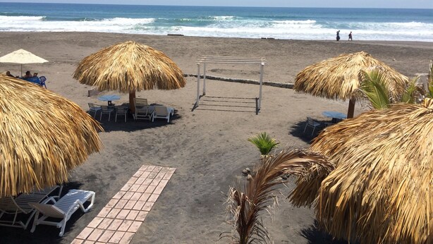 Una playa con sombrillas de paja, sillas de descanso y un camino empedrado.