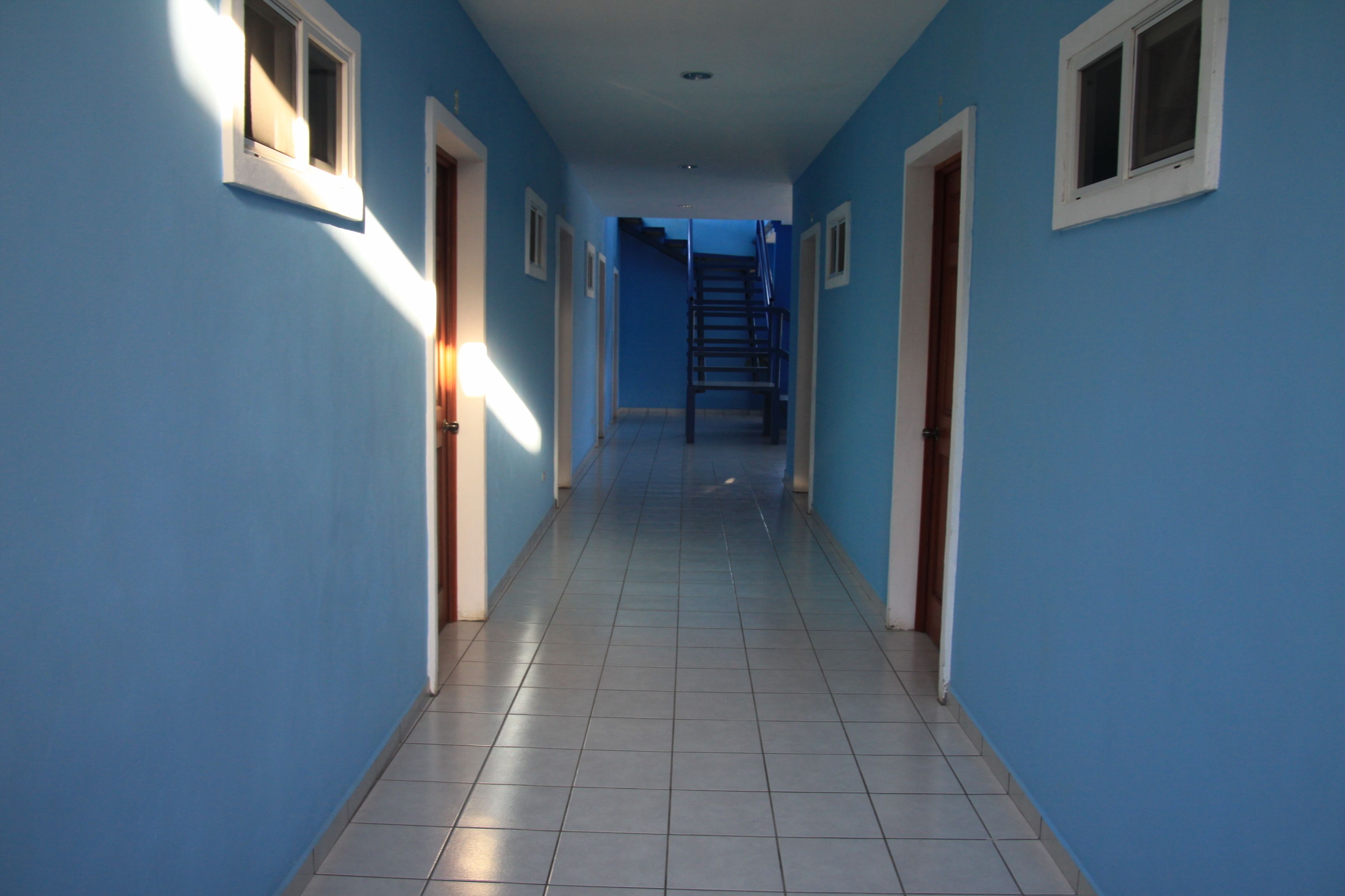 Ein langer, schmaler Flur mit blauen Wänden und weißer Verkleidung, der zu einer Treppe am Ende führt.