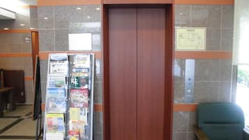 An elevator with a wooden door, a sign indicating floor 12, and a seating area with a chair to the right.