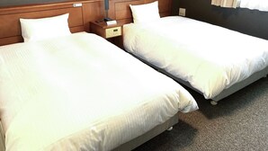 Habitación de hotel con dos camas individuales, cabecero de madera, mesita de noche con lámpara y ventana con cortinas.