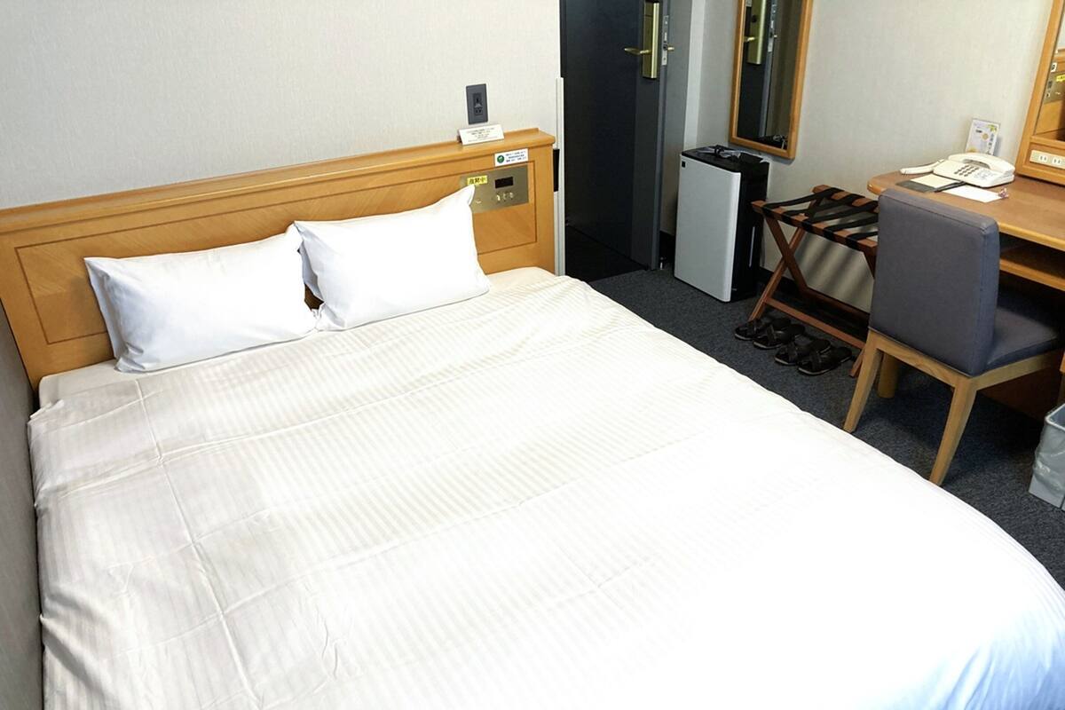 A hotel room with a large bed, a desk with a chair, a small refrigerator, and a telephone.