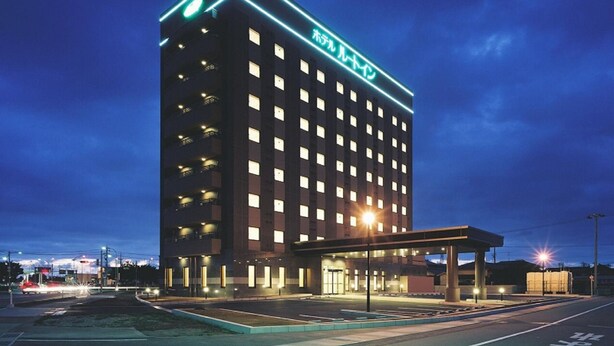 Un hotel de varios pisos con un letrero grande en la parte superior, un acceso cubierto y un área de estacionamiento al frente.