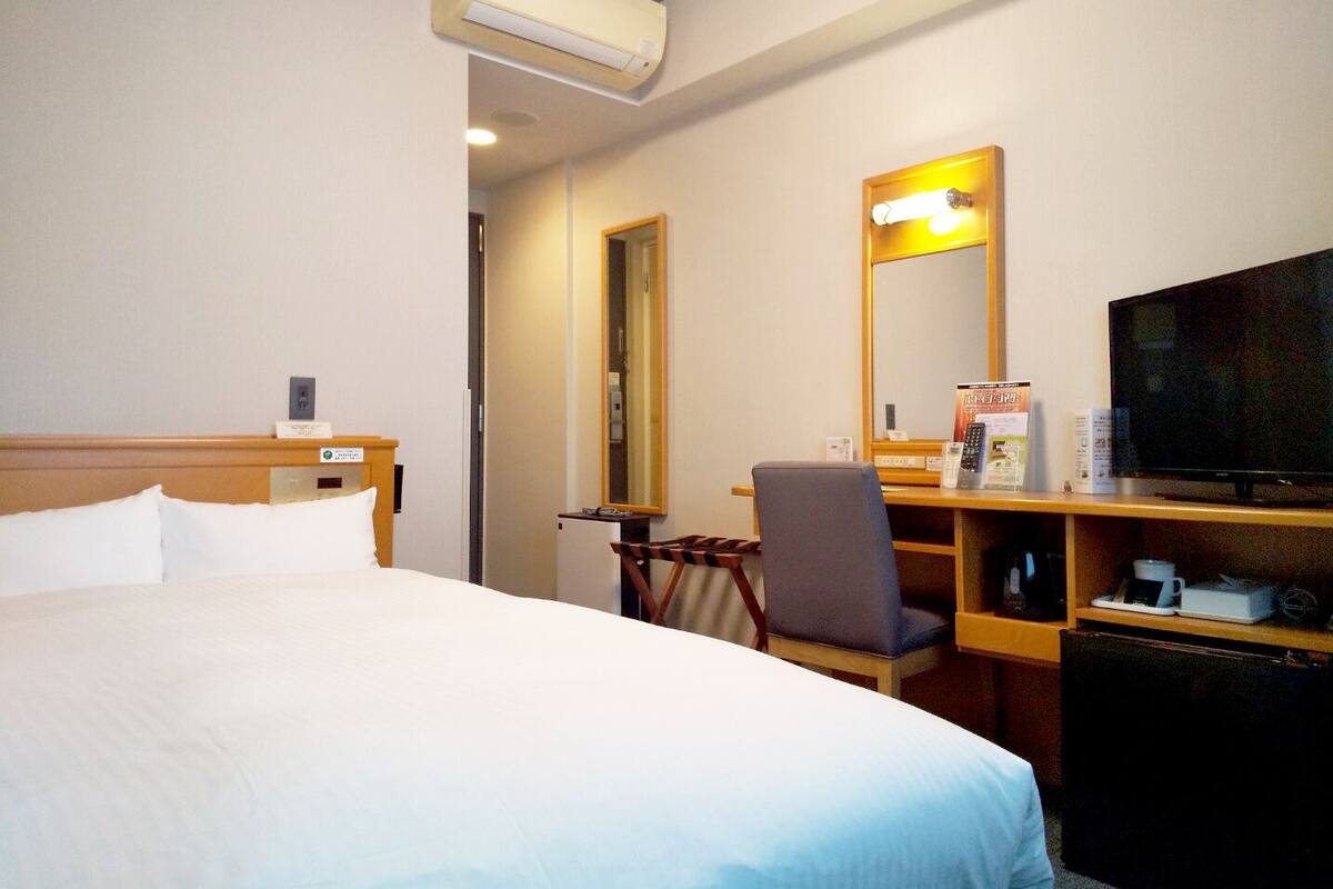 A hotel room with a bed, a desk with a chair, a television, and a mirror.