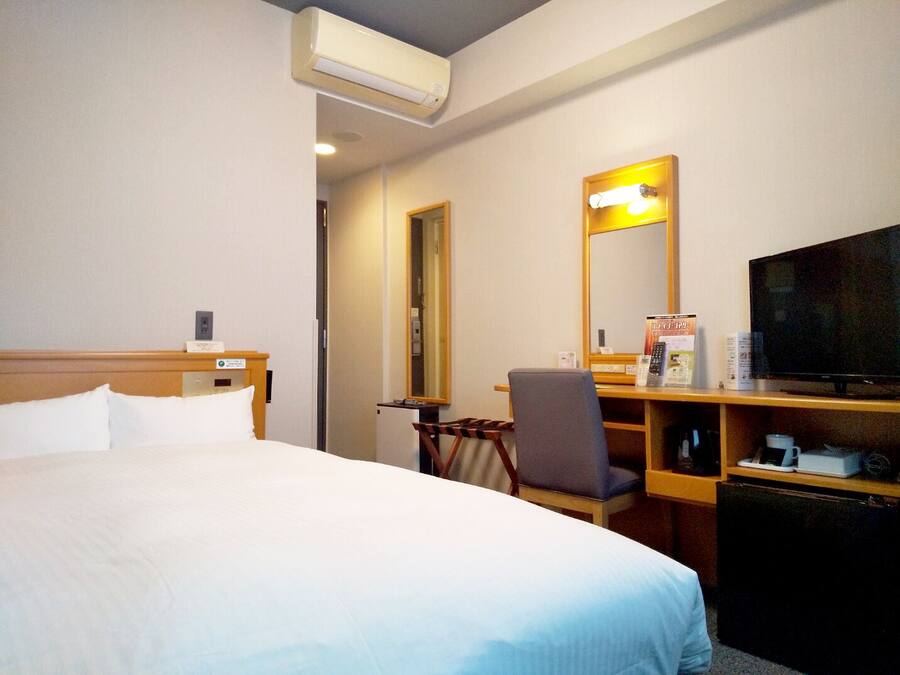 A hotel room with a bed, a desk with a chair, a television, and a mirror.