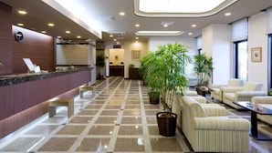 Vestíbulo de hotel con mostrador de recepción, zona de estar y plantas en macetas.
