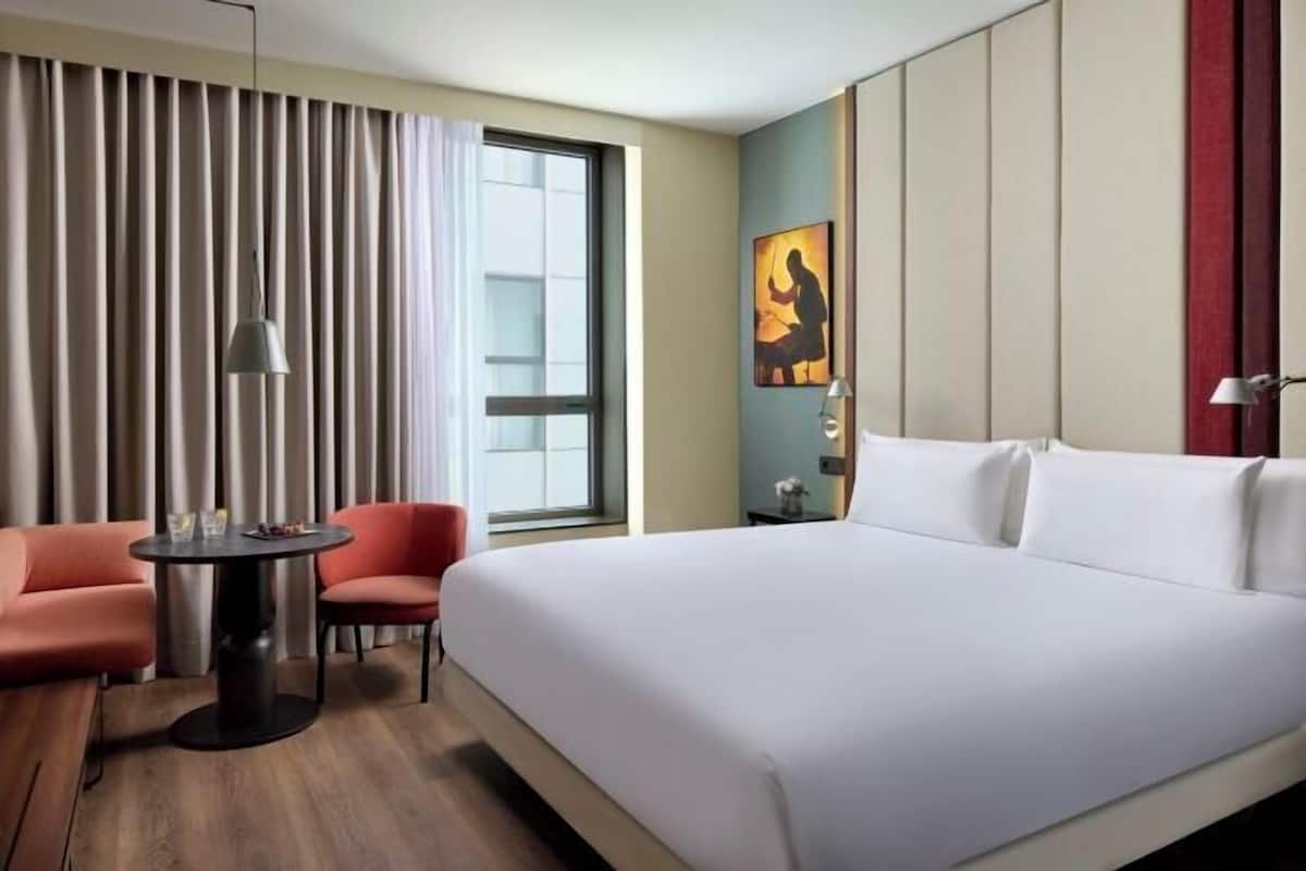 A hotel room with a large bed, a desk, a chair, a small table, and a window with curtains.