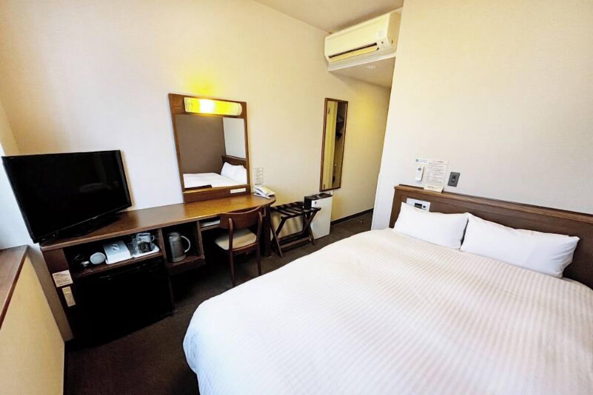 Een hotelkamer met een bed, een bureau met een televisie, een spiegel en een kleine kitchenette.