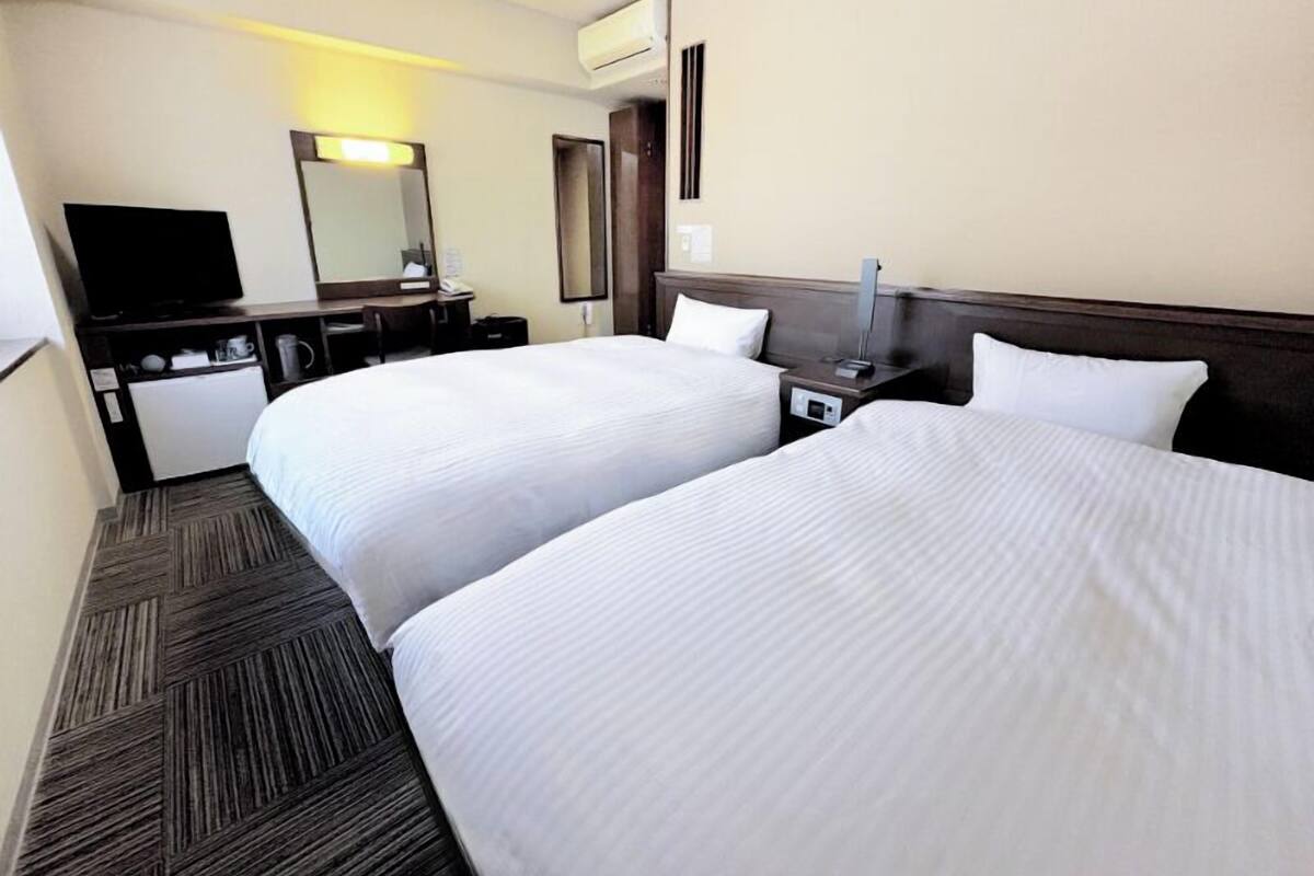 Een hotelkamer met twee bedden, een bureau, een stoel, een televisie en een airconditioning.