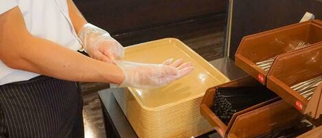 A person wearing gloves handling a large yellow container and organizing utensils in brown boxes.