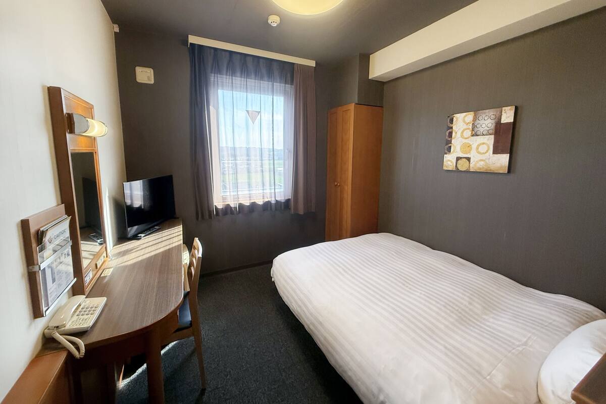 Une chambre d’hôtel comprenant un lit, un bureau avec un téléphone, une télévision, une fenêtre avec des rideaux et une œuvre d’art accrochée au mur.