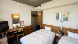 Ein Hotelzimmer mit zwei Betten, einem Schreibtisch mit Stuhl, einem Fernseher, einem Kleiderständer und einem Bild an der Wand.