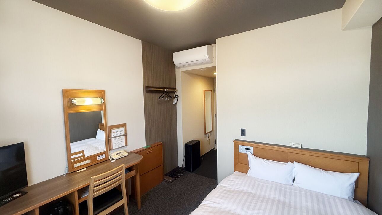 Ein Hotelzimmer mit Bett, Schreibtisch mit Stuhl, Spiegel, Fernseher und Klimaanlage.