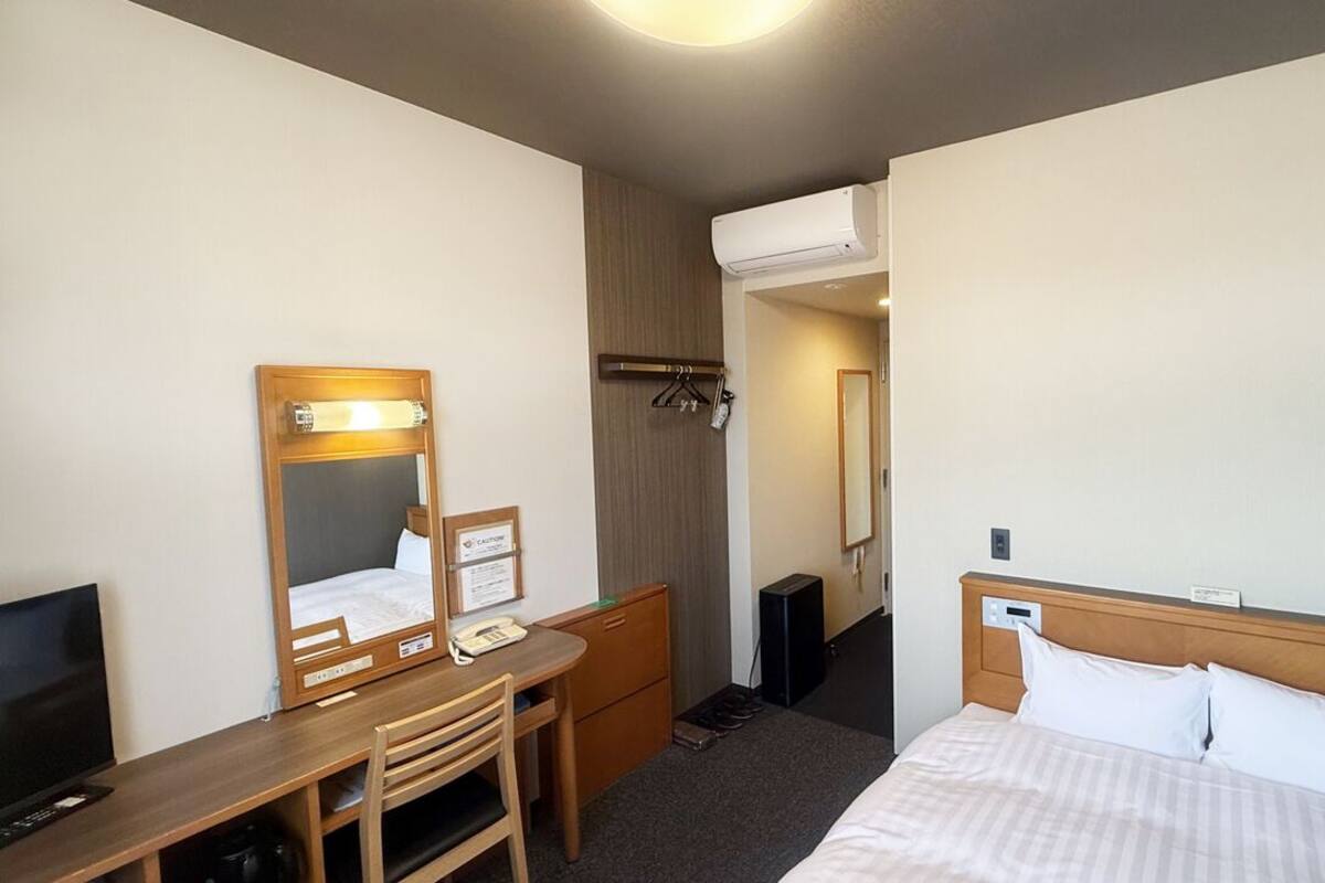 Une chambre d’hôtel équipée d’un lit, d’un bureau avec une chaise, d’un miroir, d’une télévision et d’un appareil de climatisation.
