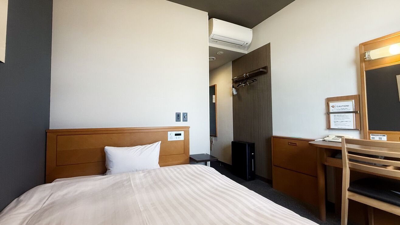 Ein Hotelzimmer mit Bett, Schreibtisch, Stuhl und Spiegel.