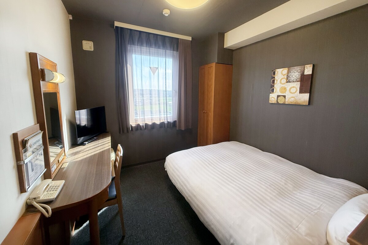 Une chambre d’hôtel comprenant un lit, un bureau avec un téléphone, une télévision, une fenêtre avec des rideaux et une œuvre d’art accrochée au mur.