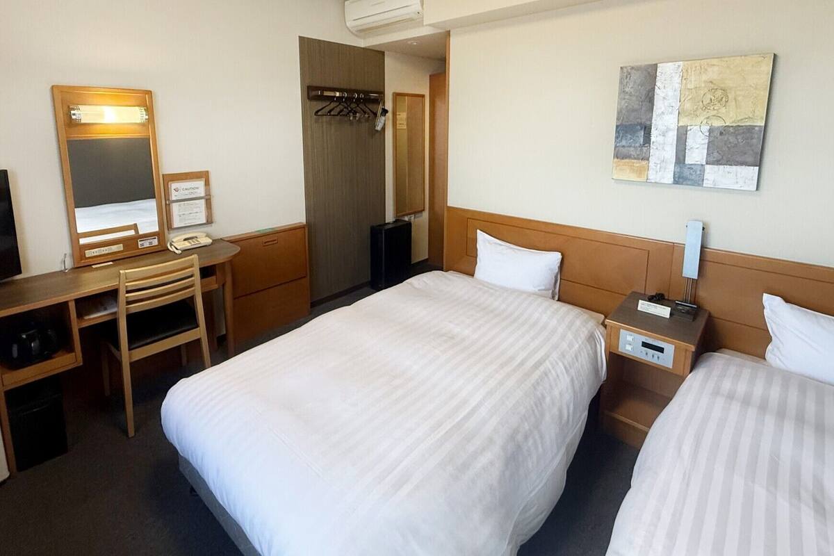 Une chambre d’hôtel avec deux lits, un bureau avec une chaise, une télévision, un miroir et une œuvre d’art accrochée au mur.