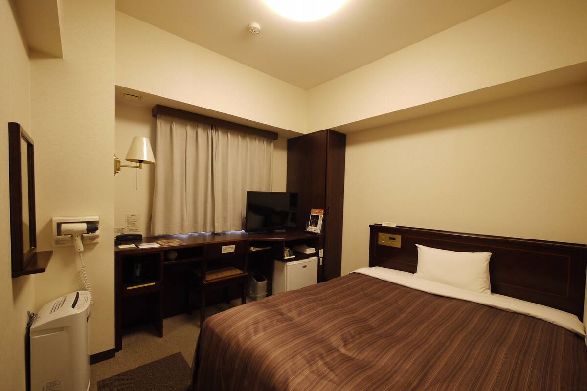 A hotel room with a bed, a desk with a computer, a TV, and a telephone.