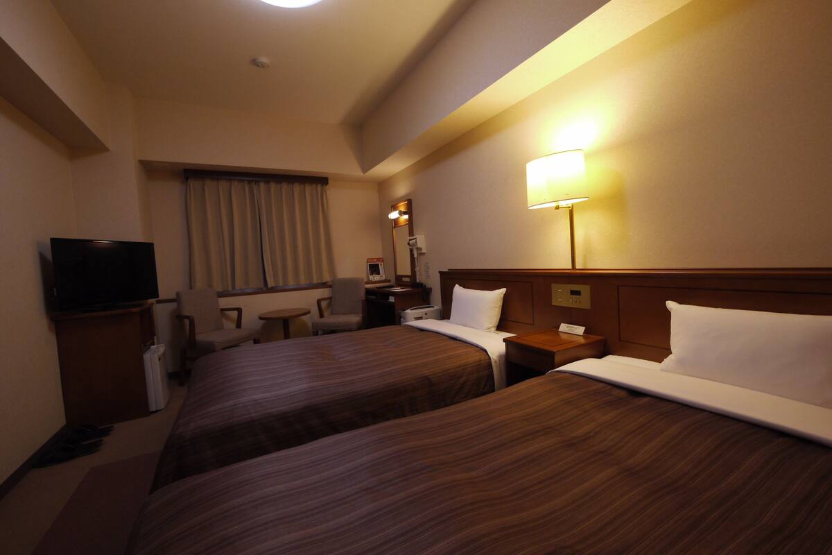 A hotel room with two beds, a TV, a desk, and a lamp.