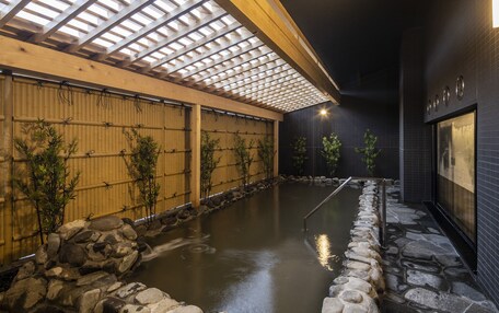 A traditional Japanese onsen with a wooden interior, stone basin, bamboo walls, and a tiled floor.