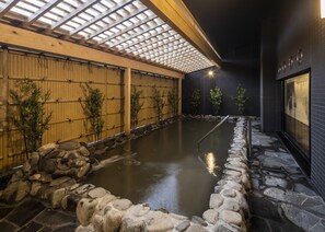 A traditional Japanese onsen with a wooden interior, stone basin, bamboo walls, and a tiled floor.