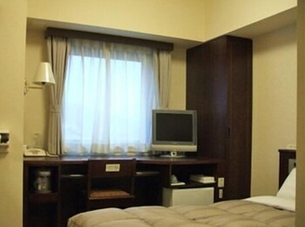 A hotel room with a bed, a desk with a television, a chair, and a window with curtains.