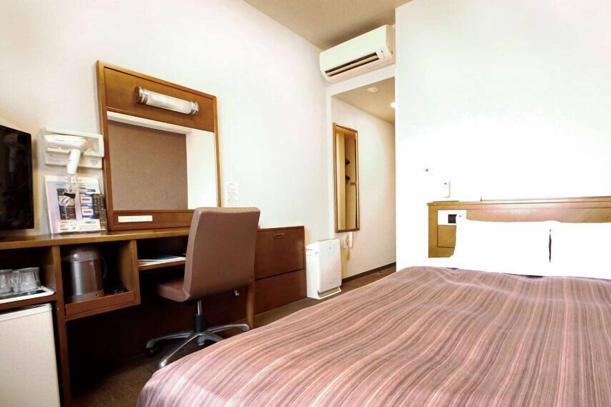 Ein Hotelzimmer mit einem Bett, einem Schreibtisch mit Stuhl, einem Spiegel, einer Klimaanlage und einer Kaffeemaschine.
