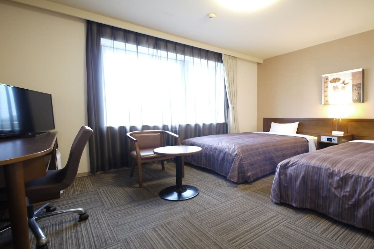Une chambre d’hôtel avec deux lits, un bureau avec une télévision, une chaise et une petite table.