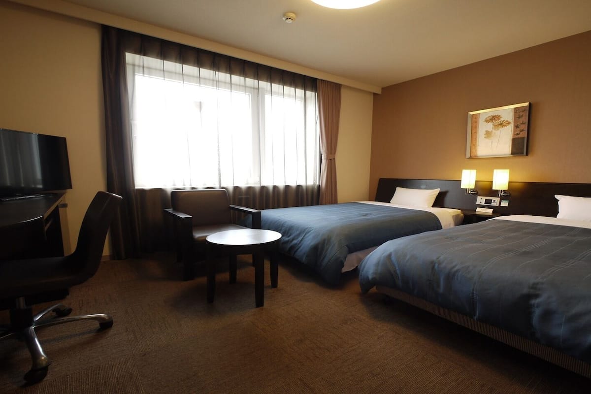Une chambre d’hôtel avec deux lits, un bureau, une chaise, une télévision et une lampe.